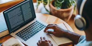 Een persoon gebruikt een laptop en luistert naar voorgelezen tekst.